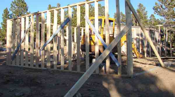 A newly raised garage wall held plumb with diagonal temporary braces and a mini excavator in the background